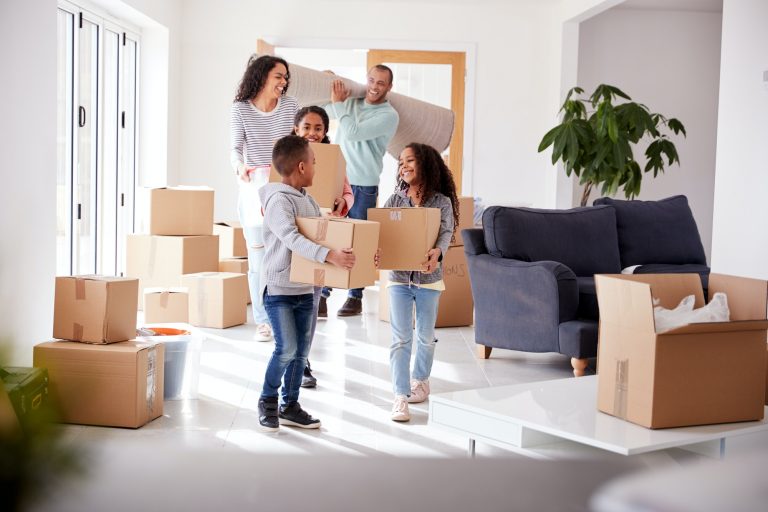 Smiling Family Carrying Boxes Into New Home On Moving Day